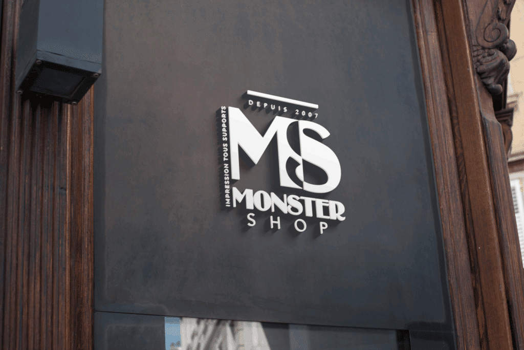 Enseigne 3D blanche "MS Monster Shop" sur façade gris anthracite. Mentions "Depuis 2007" et "Impression tous supports". Cadre en bois foncé.